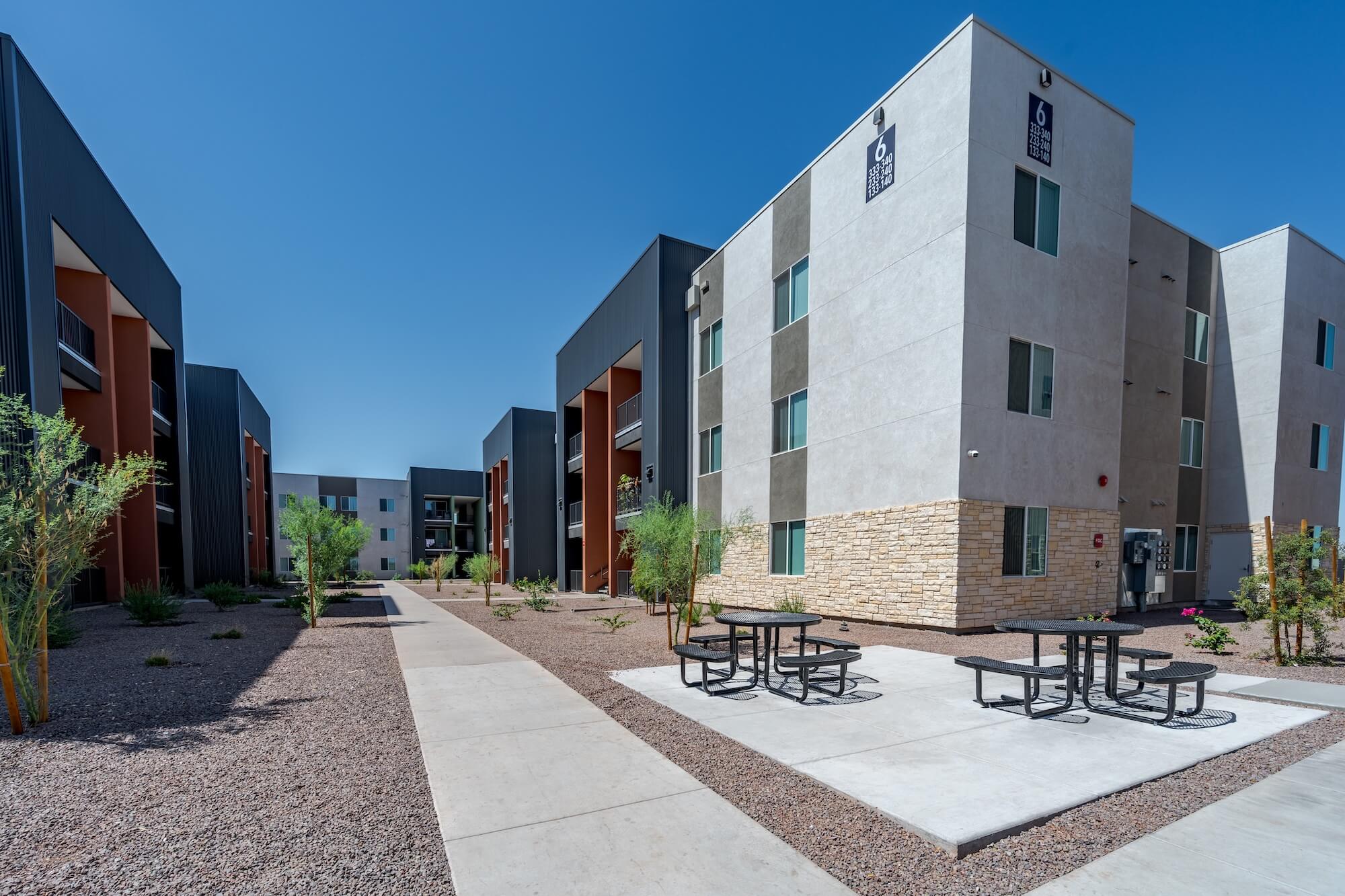 Modern apartment complex courtyard with picnic tables, desert landscaping, and clear blue sky