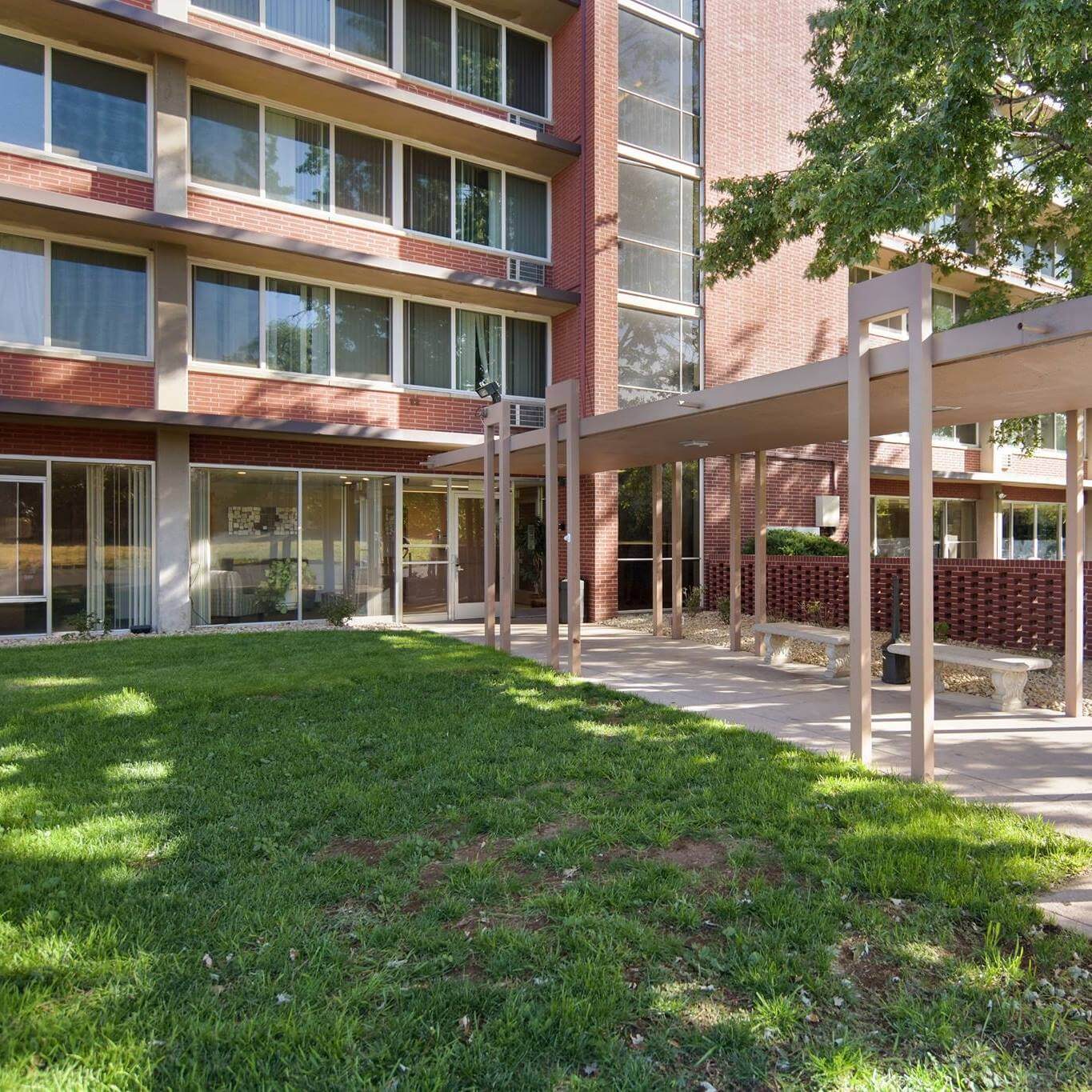 The image shows the entrance of a red-brick building, possibly Columbine Towers, with a covered walkway and green lawn.