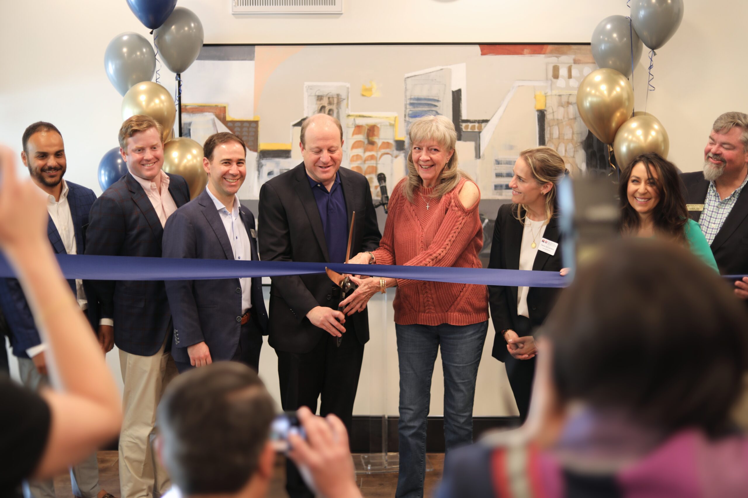 Group of people smiling during a ribbon-cutting ceremony with blue and gold balloons in the background