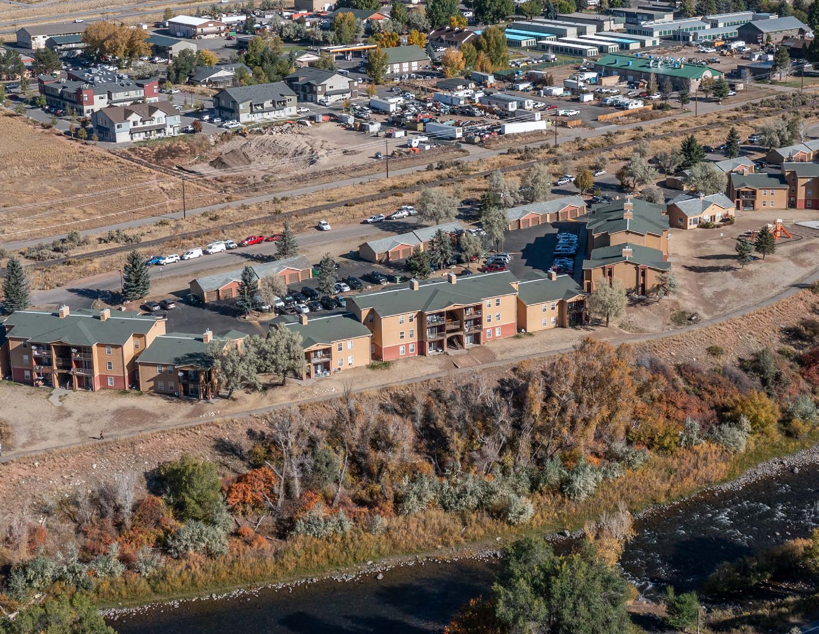 Aerial view of residential buildings with green roofs near a river, surrounded by trees and an adjacent community area