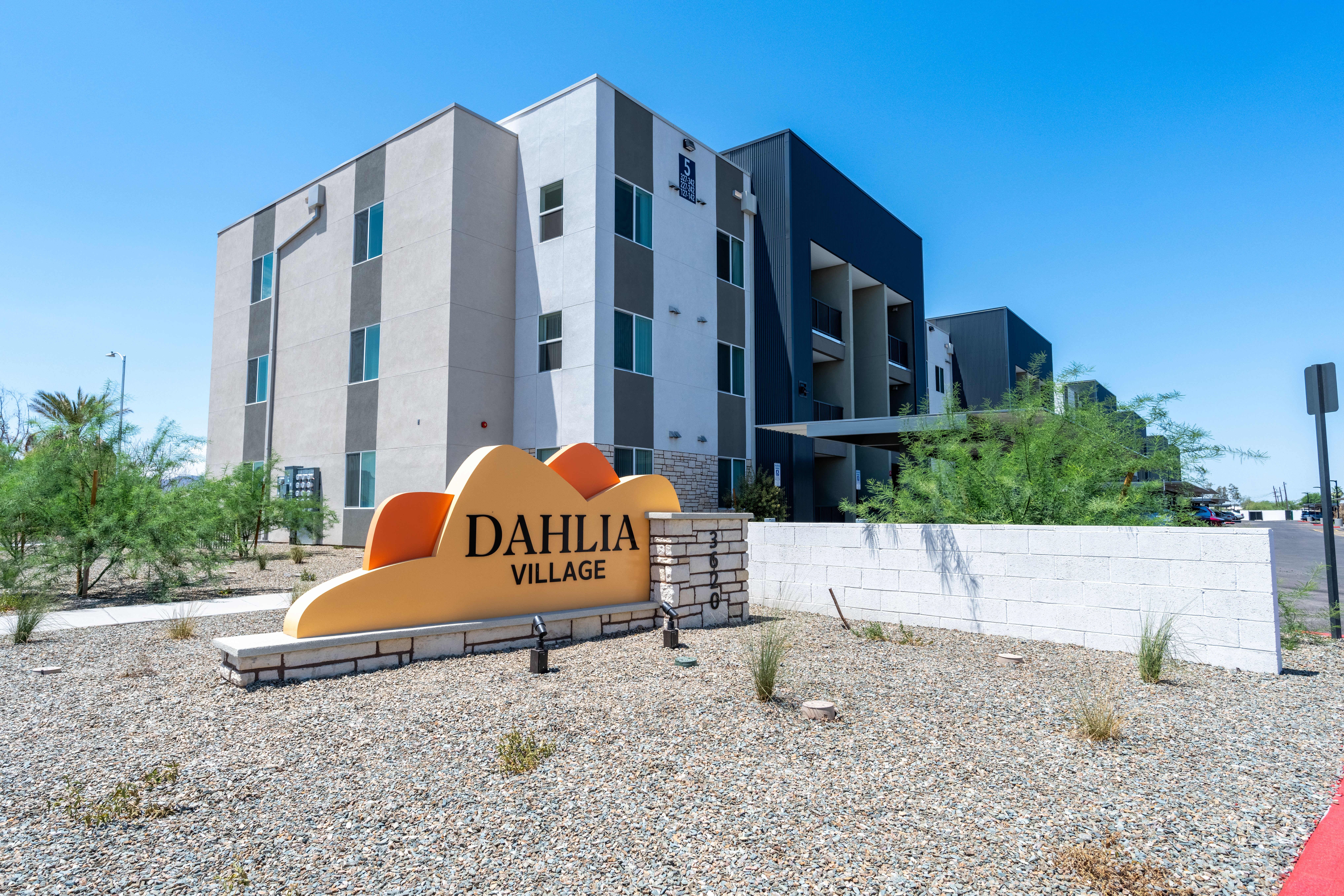 Dahlia Village sign in front of a modern apartment building under a clear blue sky