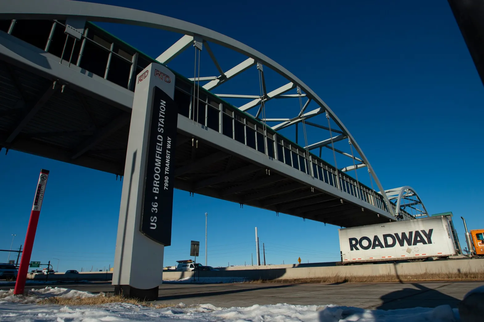 Broomfield Station sign and a bridge with blue sky, a truck with "ROADWAY" passing beneath