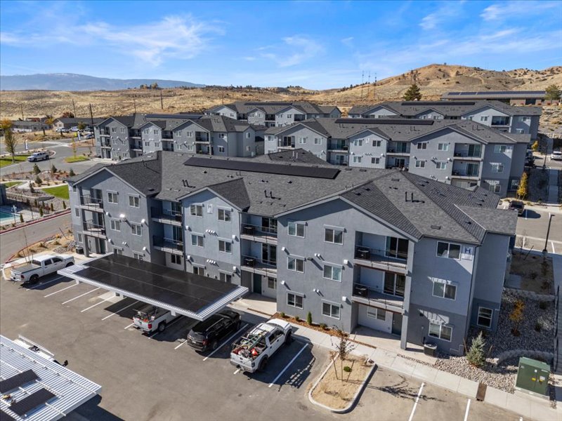 Aerial view of a large modern apartment complex with multiple three-story buildings and parking area in a hilly region