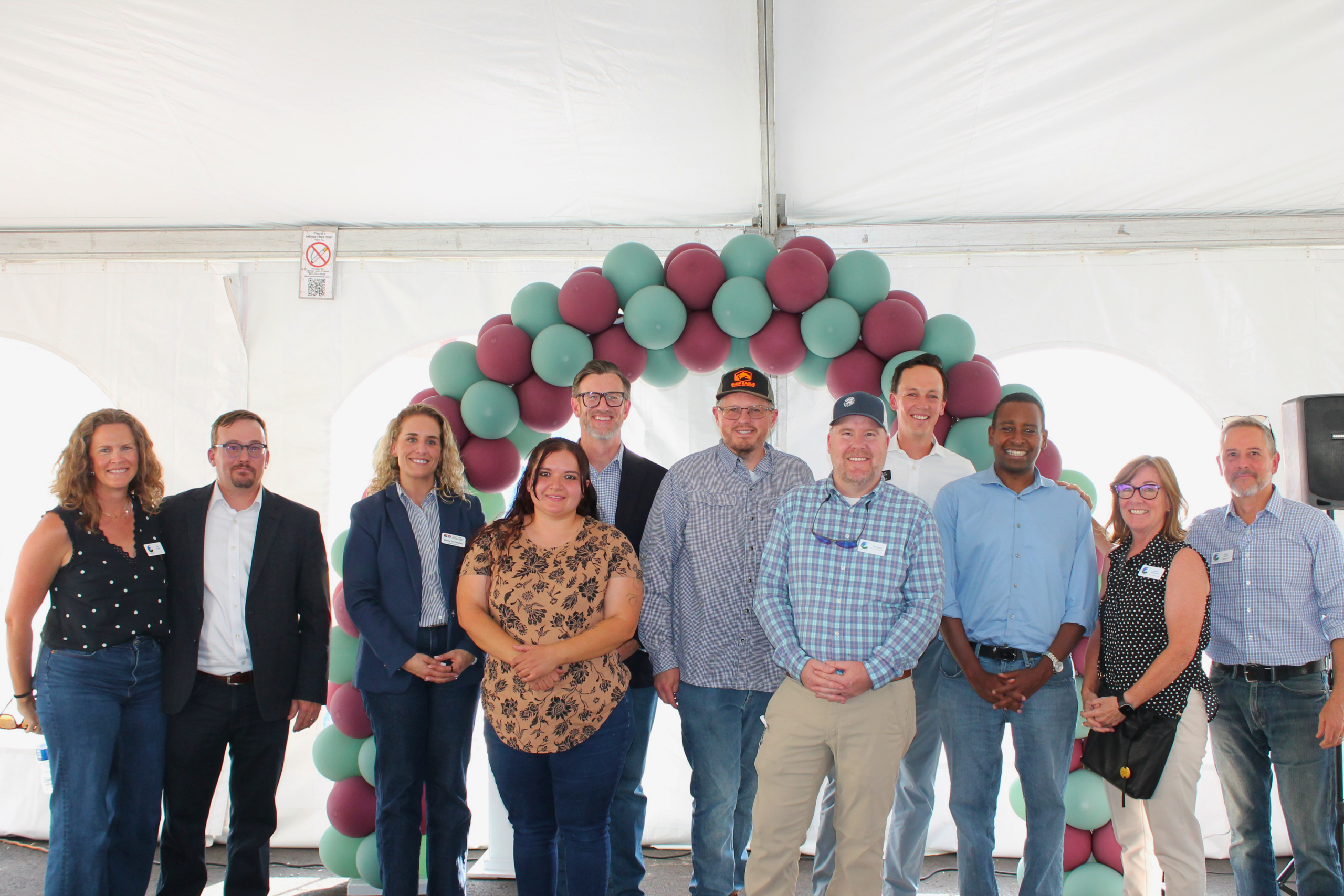 Group of ten people posing under balloon arch at an event. Everyone is smiling and wearing name badges
